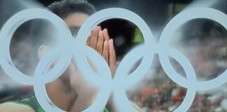 Paris 2024 Olympics: Javelin Throw Final | Pakistan’s Arshad Nadeem Wins World Record Gold A close-up photo of an athlete Arshad Nadeem with their hands covering their face, with the iconic Olympic rings blurred in the foreground. The image captures a moment of intense emotion during the Paris 2024 Olympics